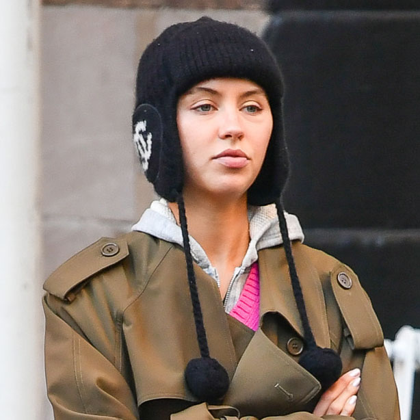 Iris Law wearing a black hat, trench coat, and red handbag