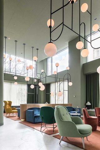 A sitting area with a variety of different chairs, round coffee tables, three pink rugs and artistic round pendant lights.