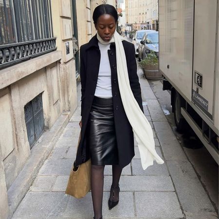 French influencer @sylviemus_ wears a black leather knee-length pencil skirt with a white top, black coat and long cream scarf.