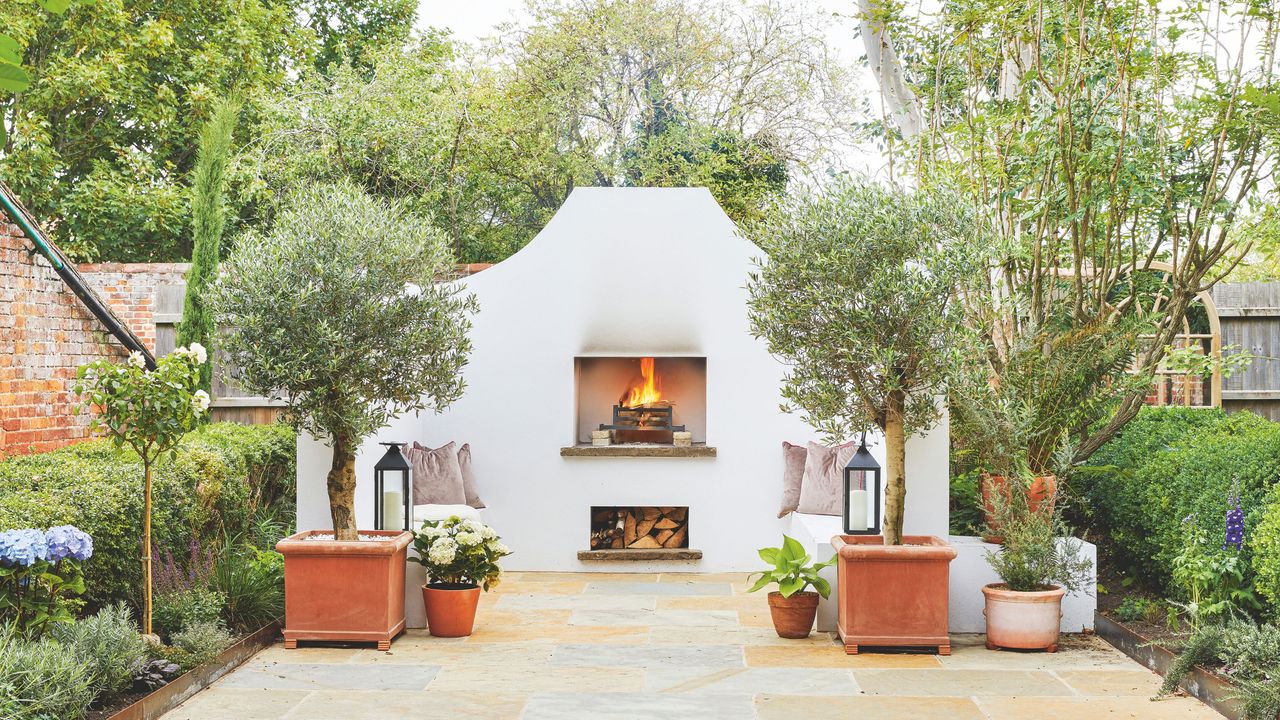 White outdoor fireplace in garden with potted trees and plants