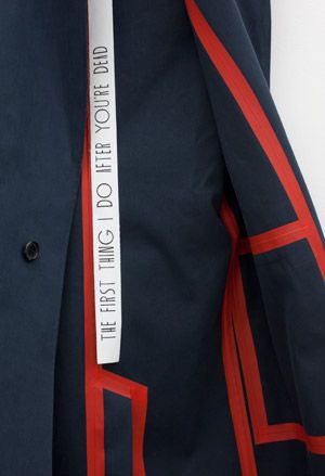 Close up view of a blue and red coat by Carlo Brandelli featuring a strip that says 'The First Thing I Do After You're Dead' at Matthew Brannon's show