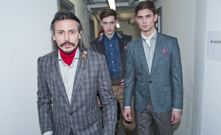 Three men in blazers looking at the camera in a narrow hallway