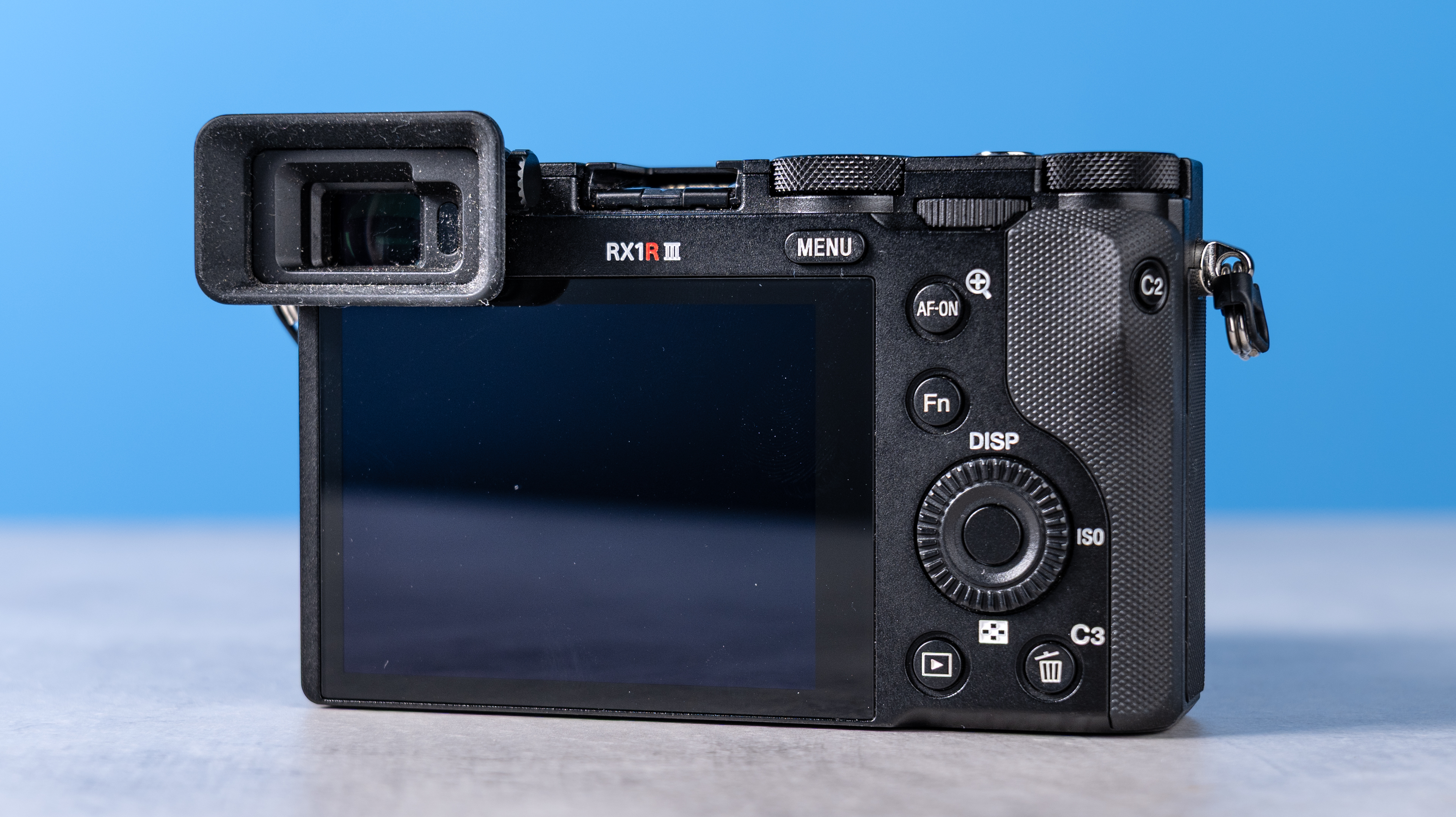 A photo of the Sony RX1R III rear. The camera on a stone surface with a blue background