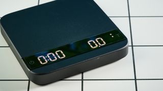 the acaia lunar coffee scale in black with an aluminum surface and accurate precise weight ideal for espresso machines given its compact size is photographed againt a blue tom's guide background