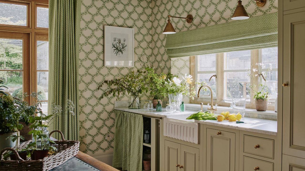 spring decorated beige shaker kitchen with a fluted sink and green decor including floral foliage wallpaper with an under sink cabinet skirt with brass wall lights