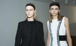 2 models wearing black headbands, black suit and white dress with black belt and grey trim