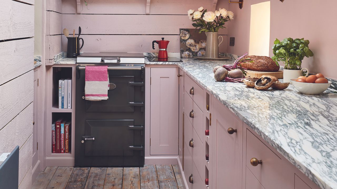 Pink shaker kitchen with marble worktops and black cooker