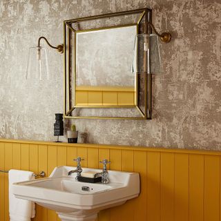bathroom with yellow painted panelling, wallpaper, wall lights, gold mirror