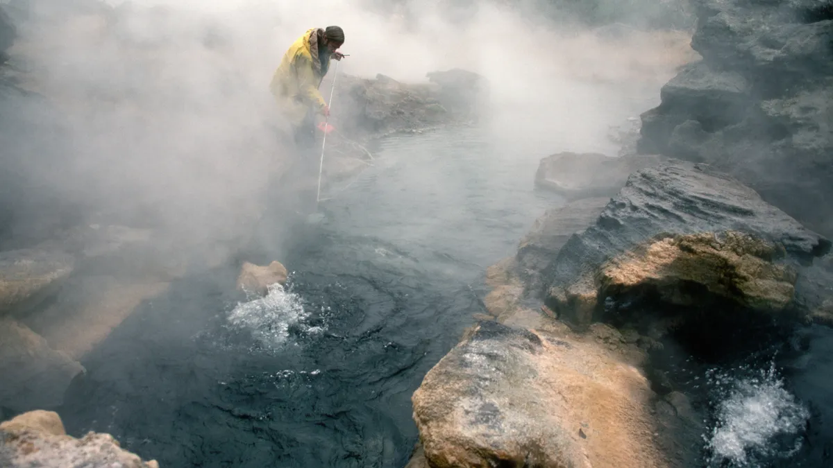 A person putting a rod in a small area of water. There is smoke around.