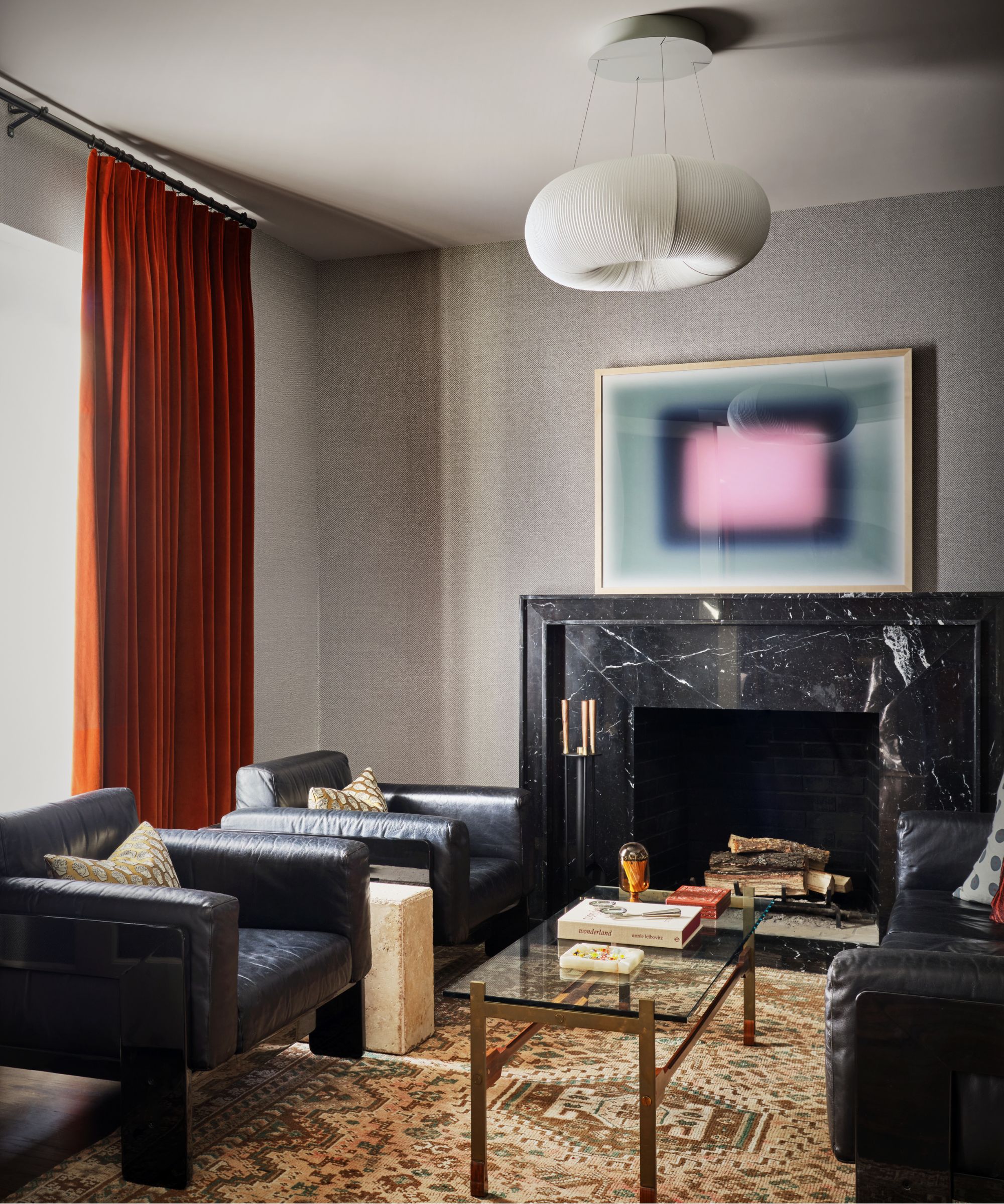 Living room with black leather armchairs, black marble fireplace, lantern pendant light, midcentury painting and tapestry carpet