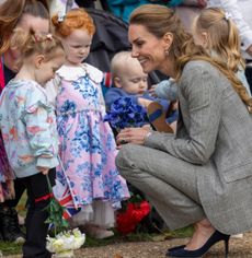 Kate Middleton kneeling down in a gray suit talking to little girls