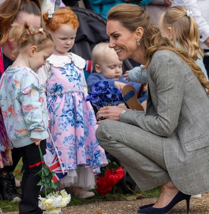 Kate Middleton kneeling down in a gray suit talking to little girls