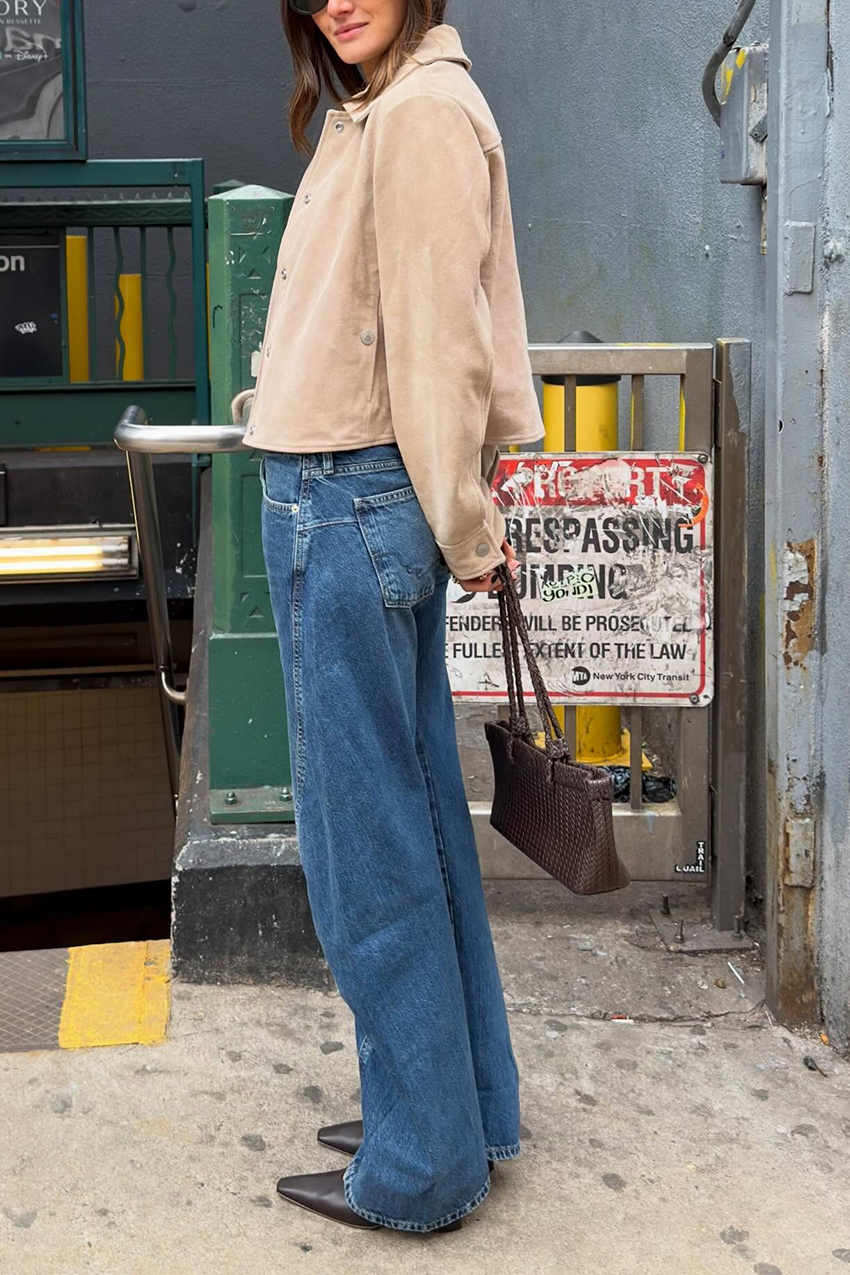 a women wearing a suede tan jacket, blue jeans, and black pointed toe boots