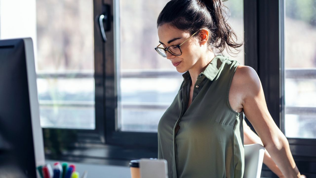 woman at a work desk doing a chest stretch with hands interlocked and arms extended behind her