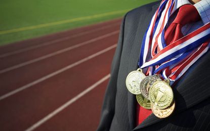 Businessman stands draped with gold, silver, and bronze medals with a running track in the background