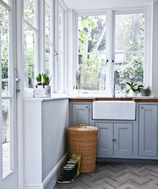 Laundry room ideas with large windows filling the upper half of the room, white painted walls and gray cabinetry with a tall wicker laundry basket in front.