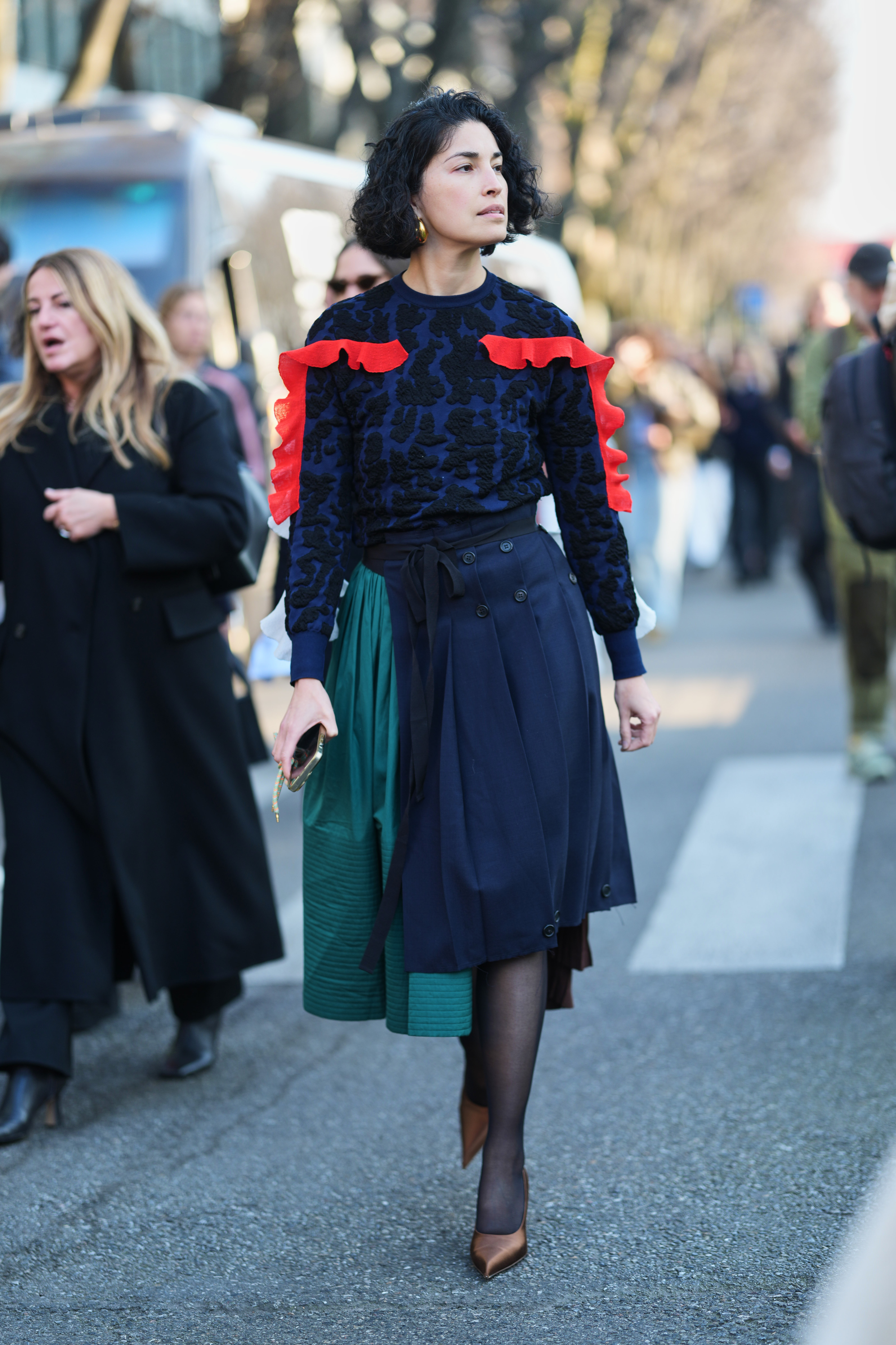 a woman wearing a navy and red sweater, and green and navy kilt skirt, and brown satin heels