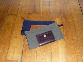 A small navy blue zip pencil-case bag resting under a grey zip pencil-case with a dark brown centre piece.