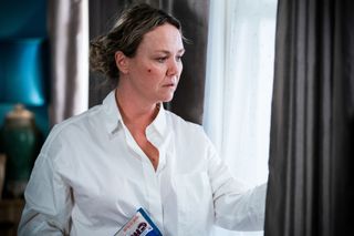 Janine Butcher sees something suspicious wile looking out a window and wearing a white shirt in EastEnders