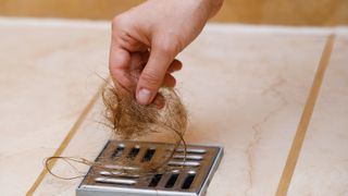 A hand removing hair from a shower drain