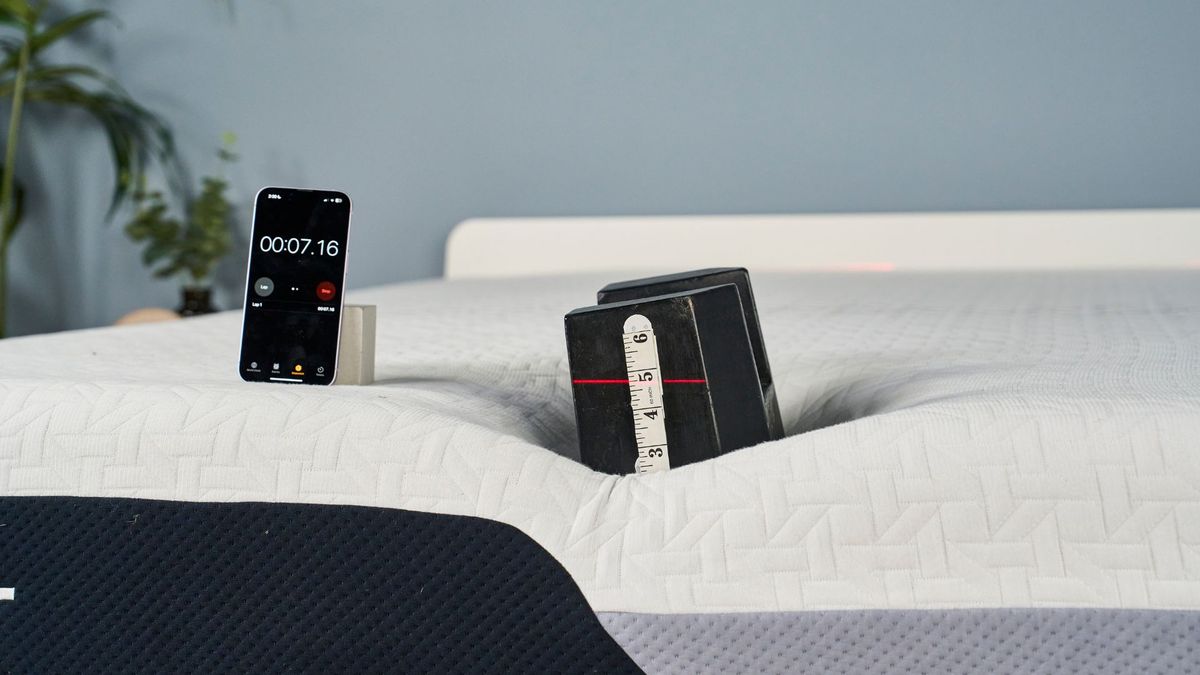 A 25kg is balanced on the edge of the Nectar Premier Memory Foam Mattress to test how far it sinks into the foam surface. A red laser line hits the weight's inch markers to pinpoint how deep the weight is sinking into the mattress's surface.
