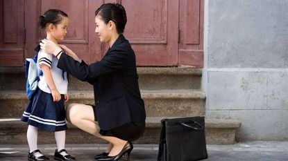 A mom in a business suit and briefcase gets her daughter ready for school.