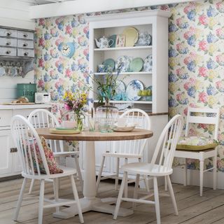 Dining area in kitchen with white furniture, floral wallpaper and tall sideboard