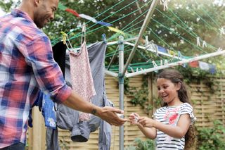 father and daughter hanging clothes on a rotary washing line in the garden