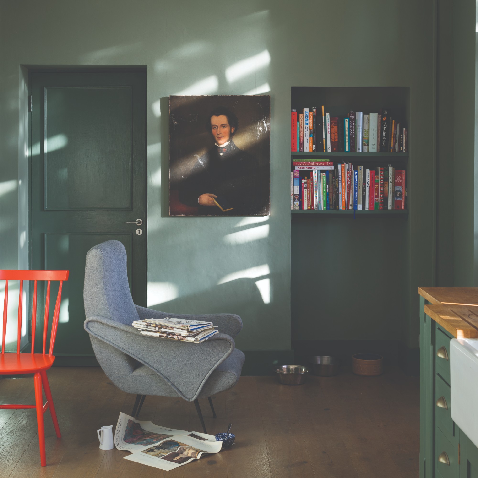 A kitchen painted in Farrow & Ball's Green Smoke paint with a green armchair