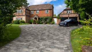 grey paved driveway leading to large country house with car in drive