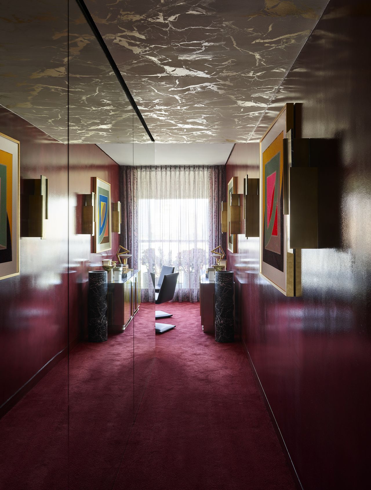 opulent hallway with mirrored wall, patterned ceiling, and plum colored carpets, artwork on wall