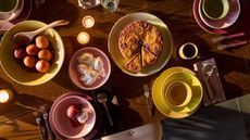 Aerial view of dark wood dining table with a breakfast spread served on yellow and pink ceramic tableware