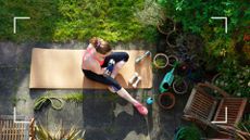Woman exercising in back garden with one of the best workout apps, using yoga mat and dumbells, surrounded by garden furniture and grass