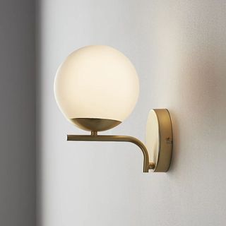 A modern wall light with a large spherical bulb and brushed brass body 