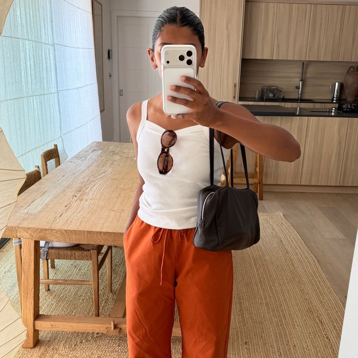 @monikh taking a mirror selfie wearing orange trousers and white vest