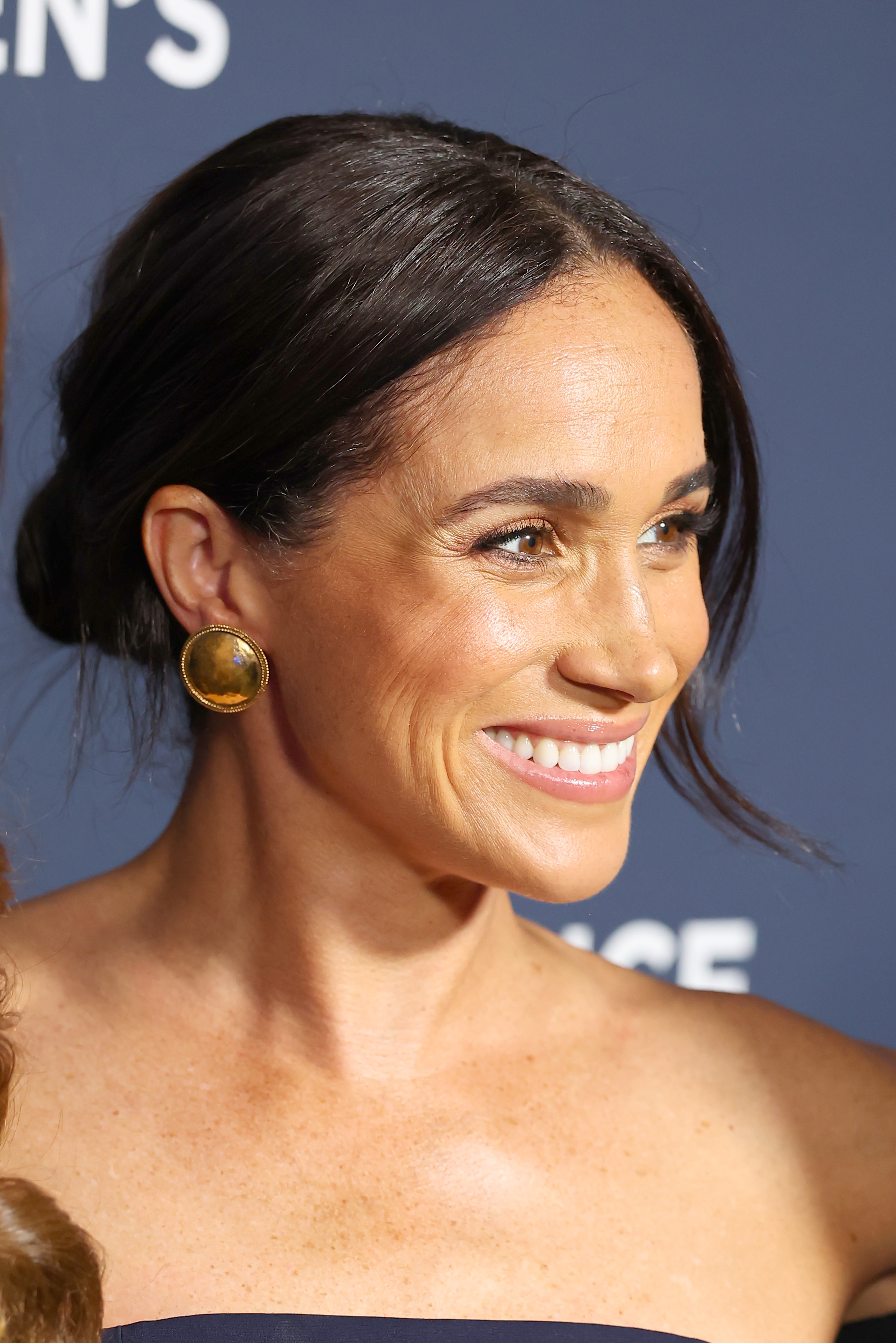 Meghan Markle smiling wearing gold earrings and a strapless dress