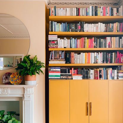 Yellow bookcases beside fireplace and round mirror