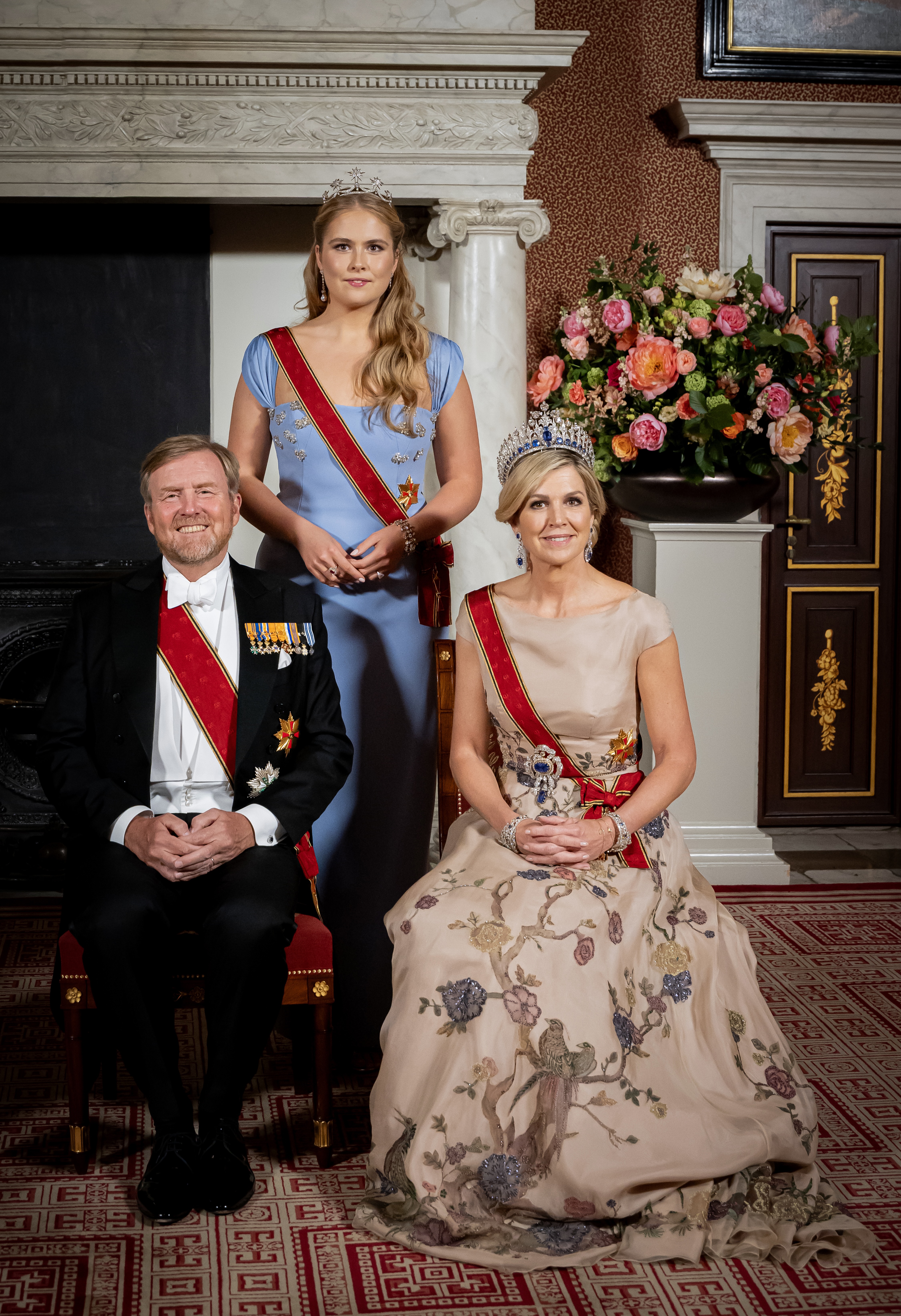 Princess Catharina Amalia, Queen Maxima and King Willem-Alexander posing in front of a fireplace