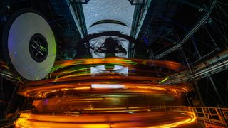A long exposure image shows rings of glowing lights inside the dome of an observatory with streaks through the open dome showing the stars