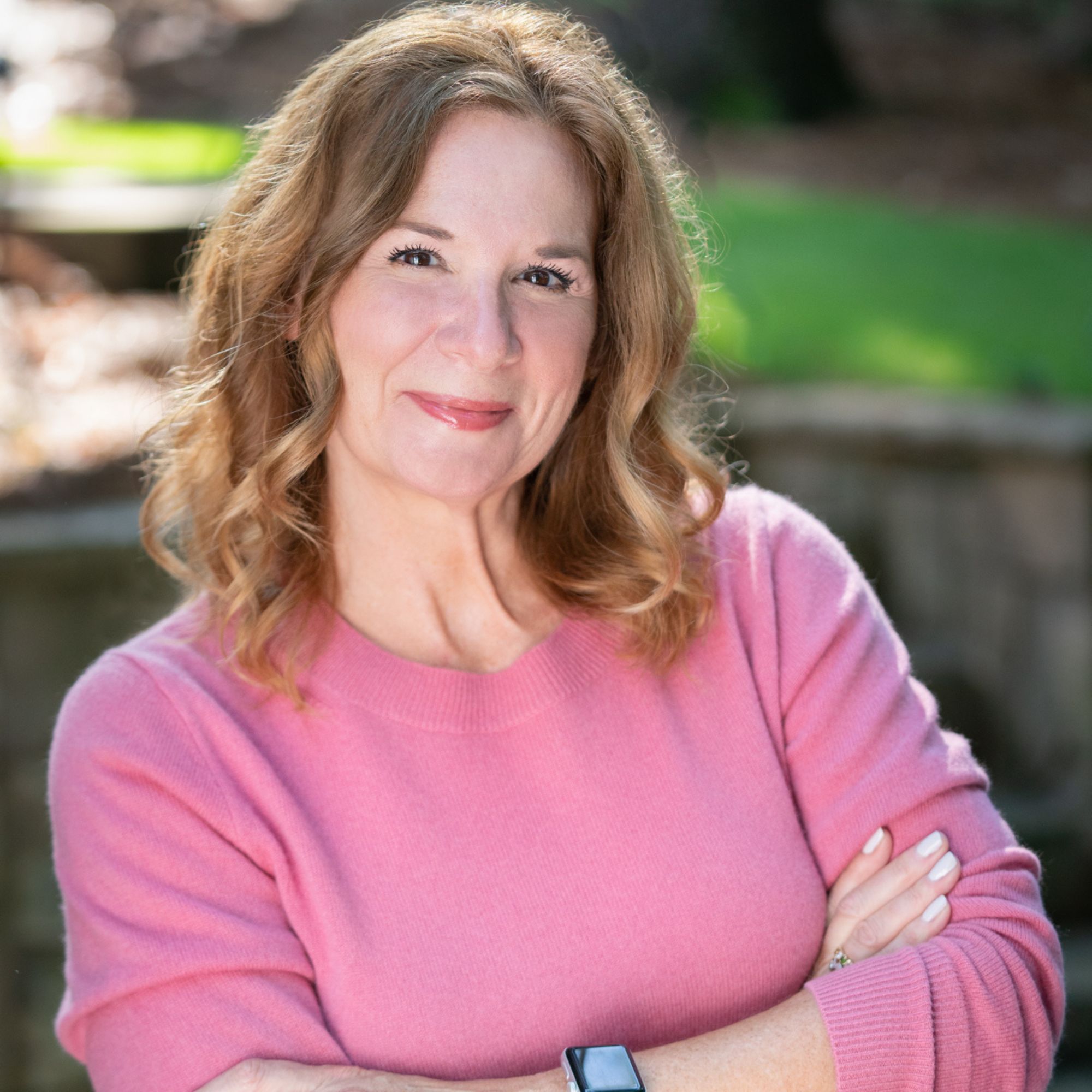 Jeannine Janoit with her arms crossed, smiling while wearing a pink jumper