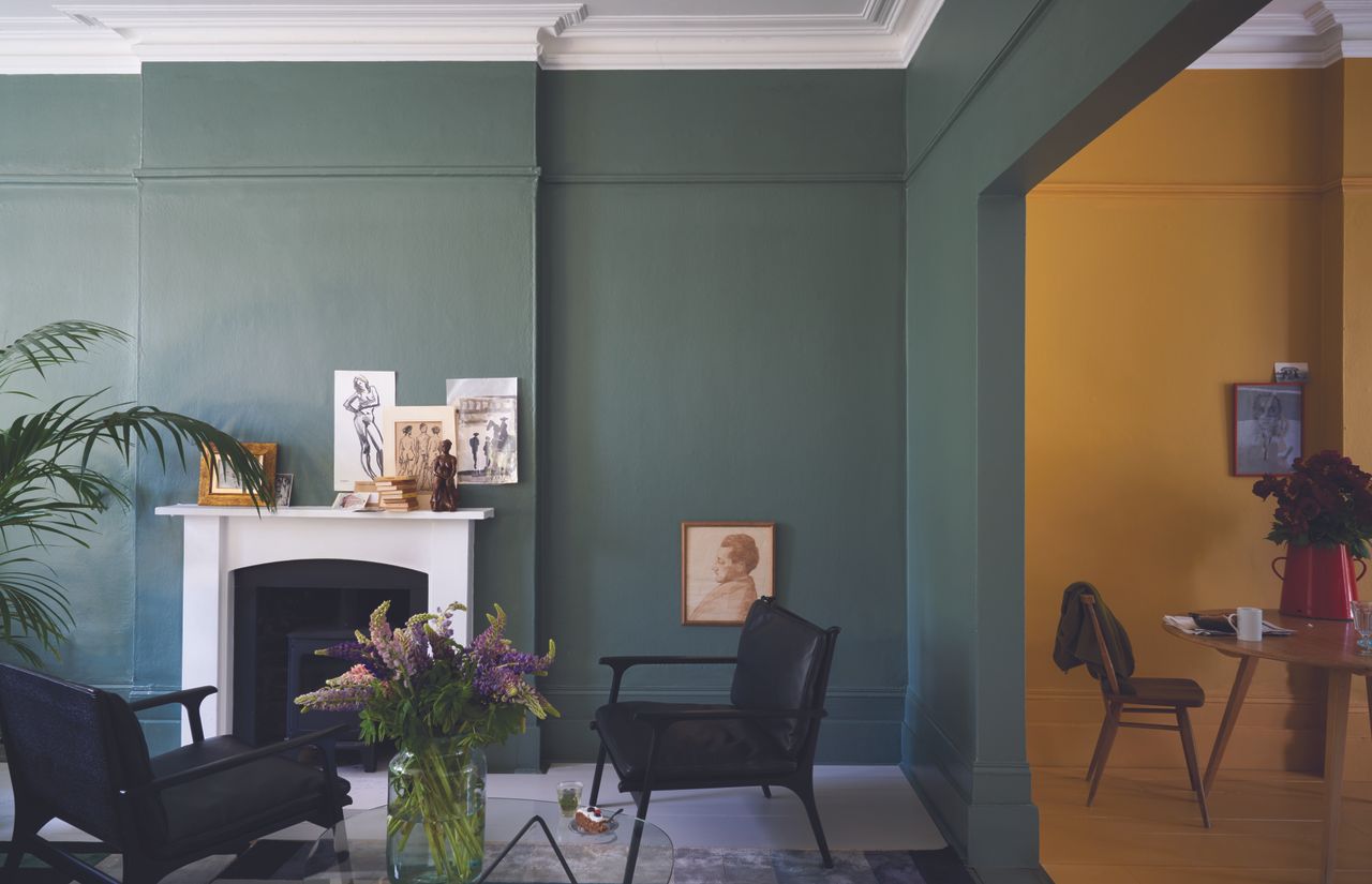 A living room with a fireplace with sage green walls and an adjoining room painted in a warm yellow shade