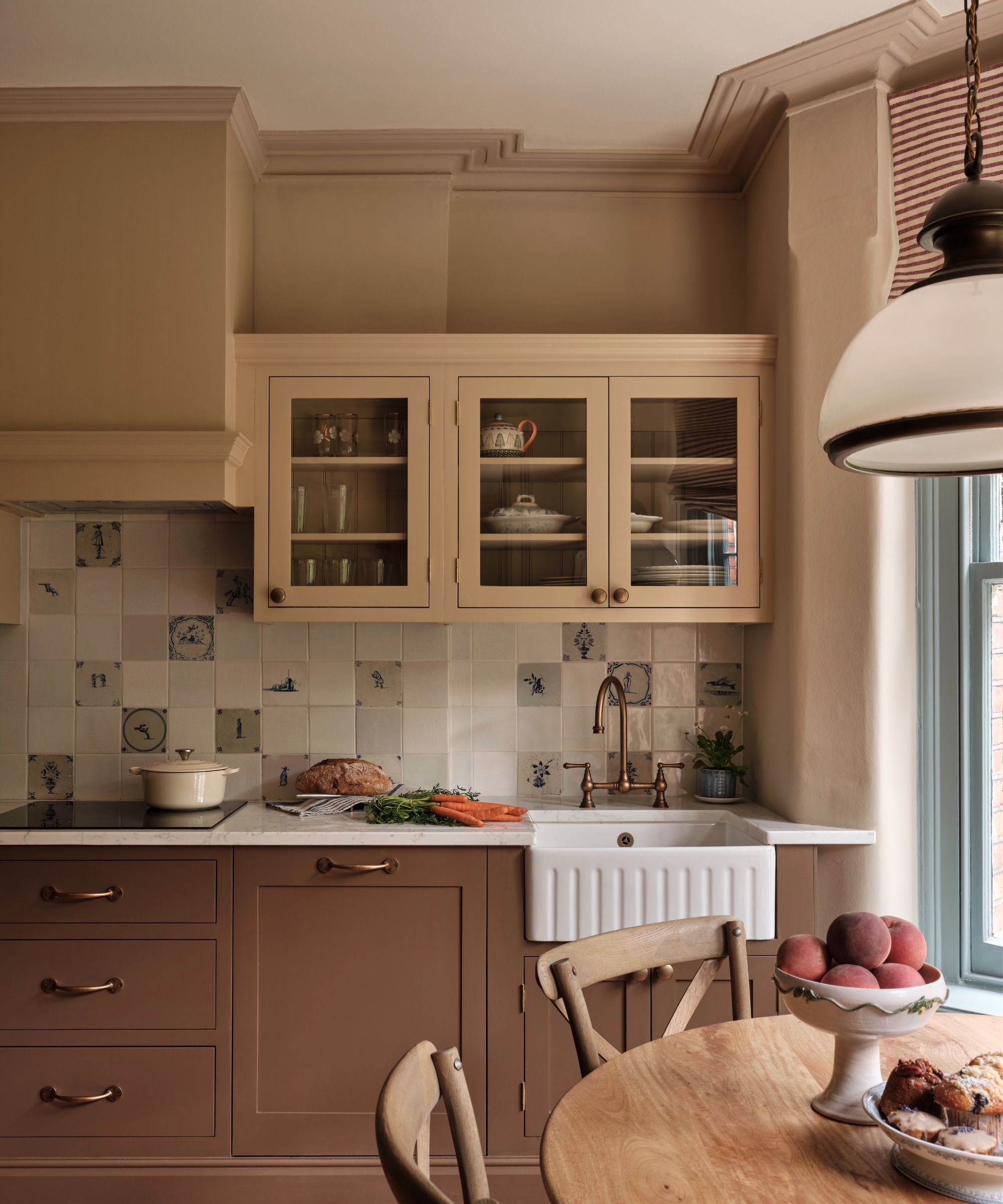 Chocolate brown kitchen cabinets paired with beige upper cabinetry, pale blue accents, Delft-style tiles, and brass hardware in a traditional kitchen.