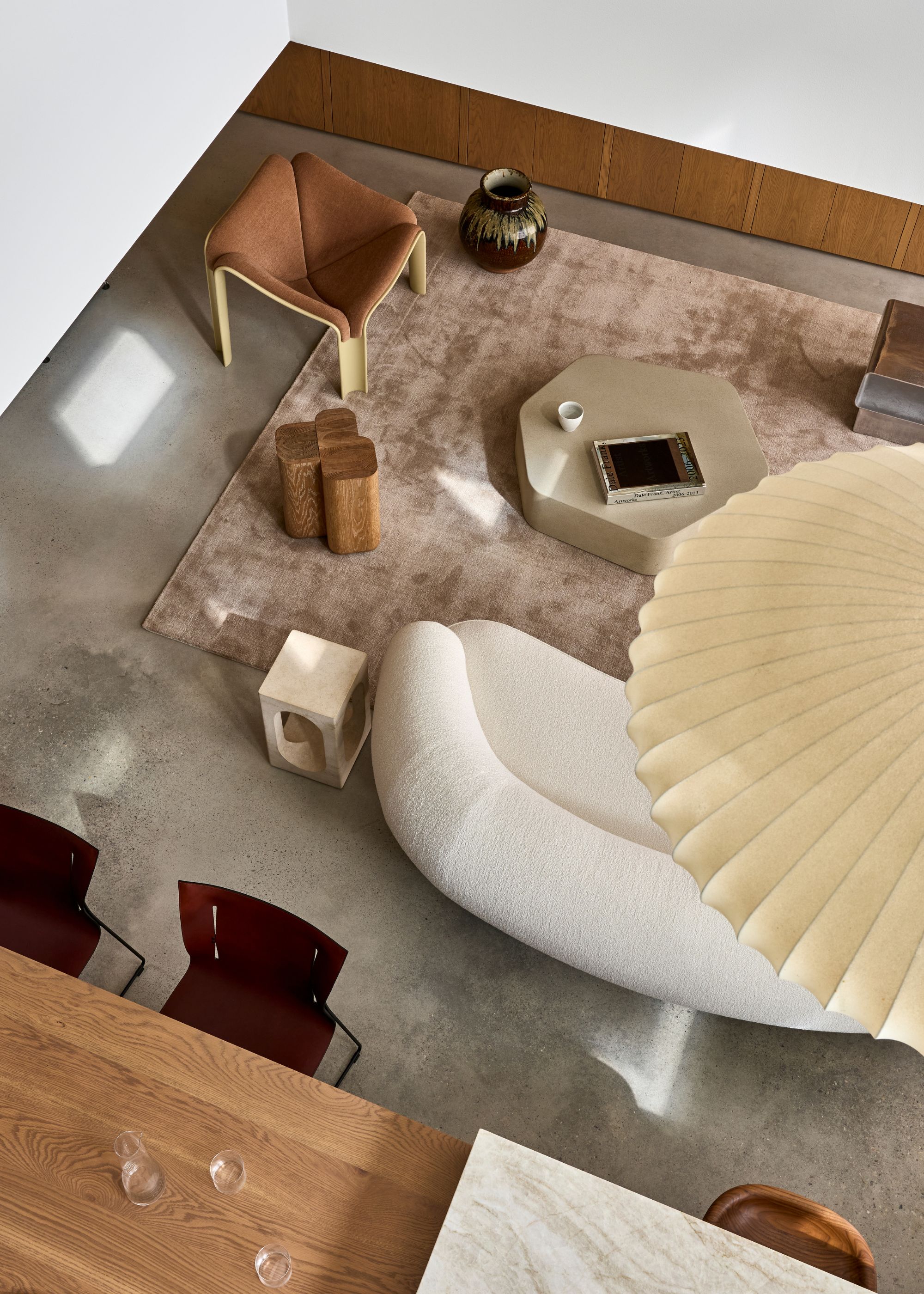 An overhead view of a living room with a pleated pendant, a white sofa, a brown chair, a beige coffee table, red dining chairs, and an area rug