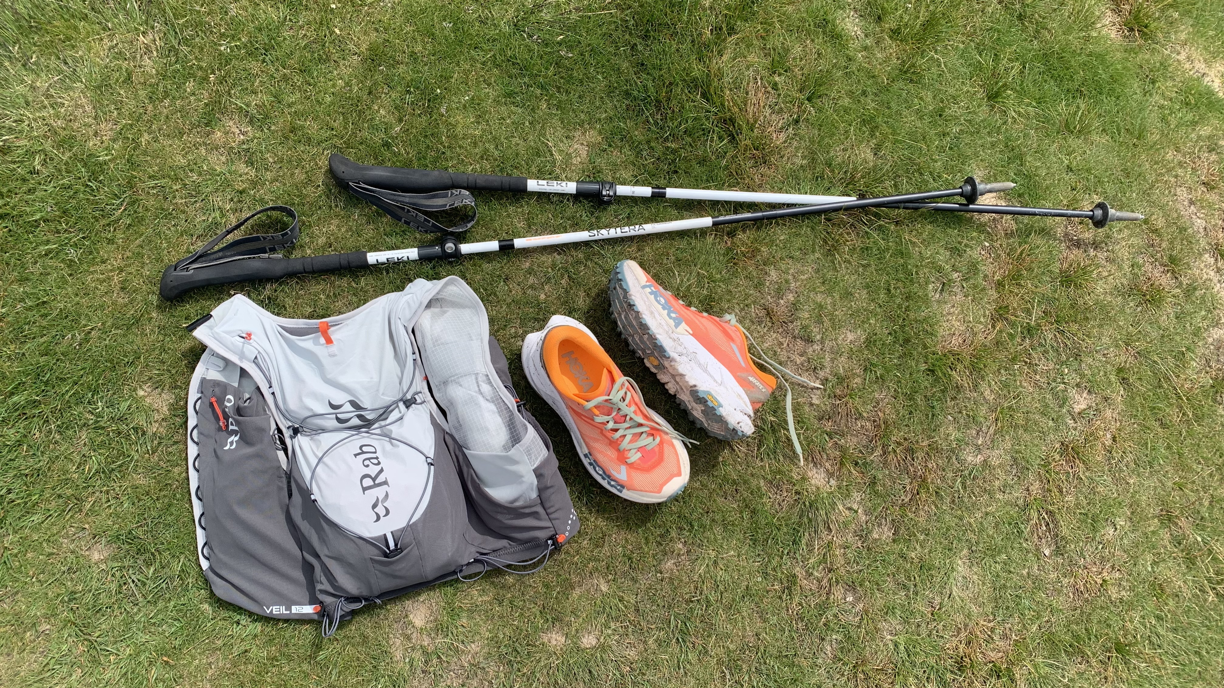 Rab Veil 12L Lightweight Running Vest lying on the ground next trail running shoes and poles