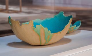 A smashed bowl in pale orange, with the blue and green inside part that bleeds over the uneven edge.