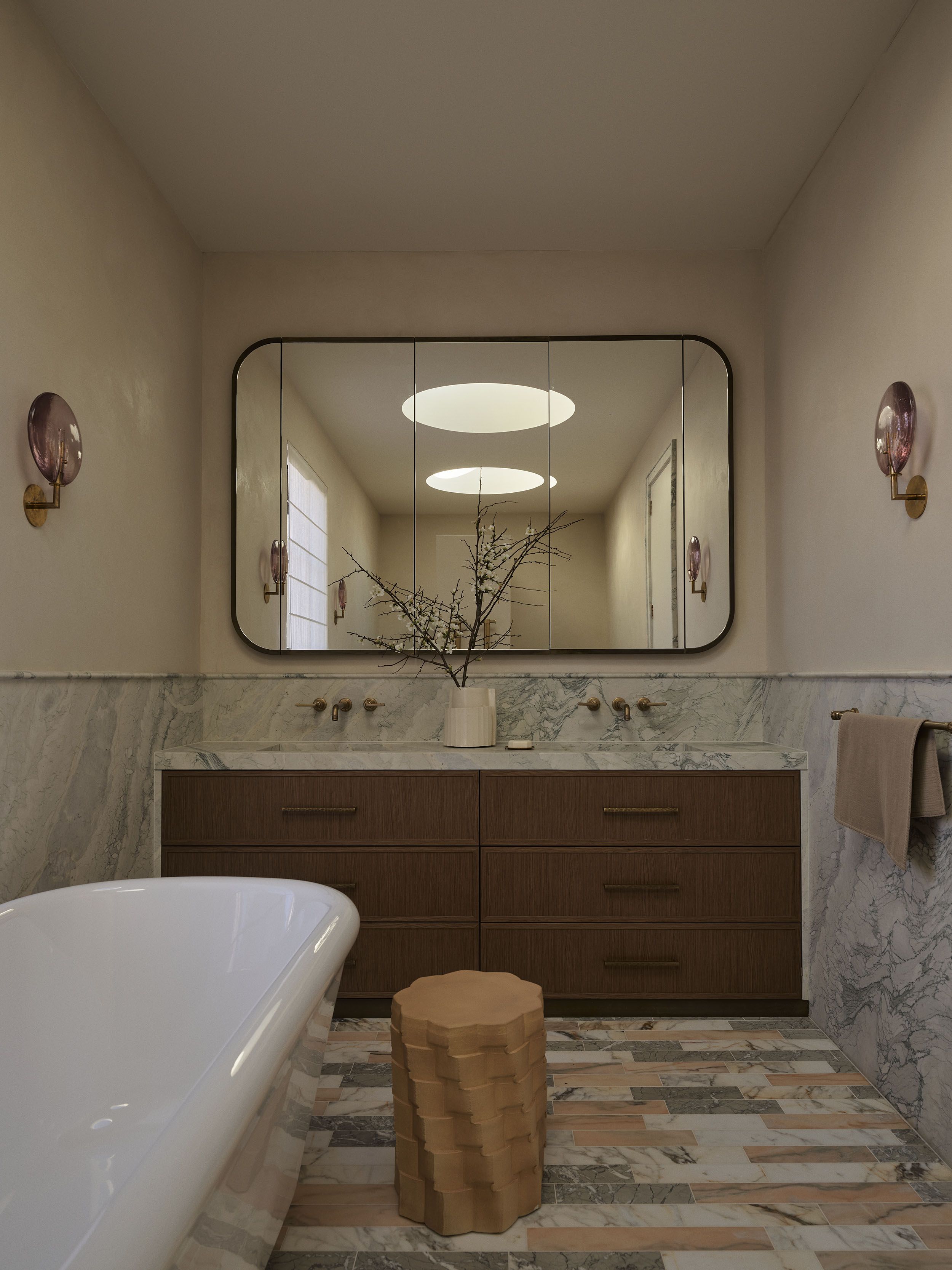 Primary bathroom featuring twin marble vanities, rounded mirrors, circular skylights and handcrafted timber cabinetry in Smac Studio's Woollahra home.