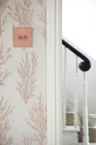 light switch in living room with pink and white wallpaper looking through the door to the staircase