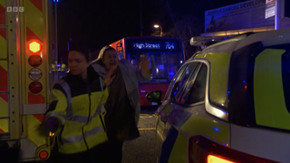 Bernie Taylor looks hysterical as she helps a paramedic with ambulances in the background