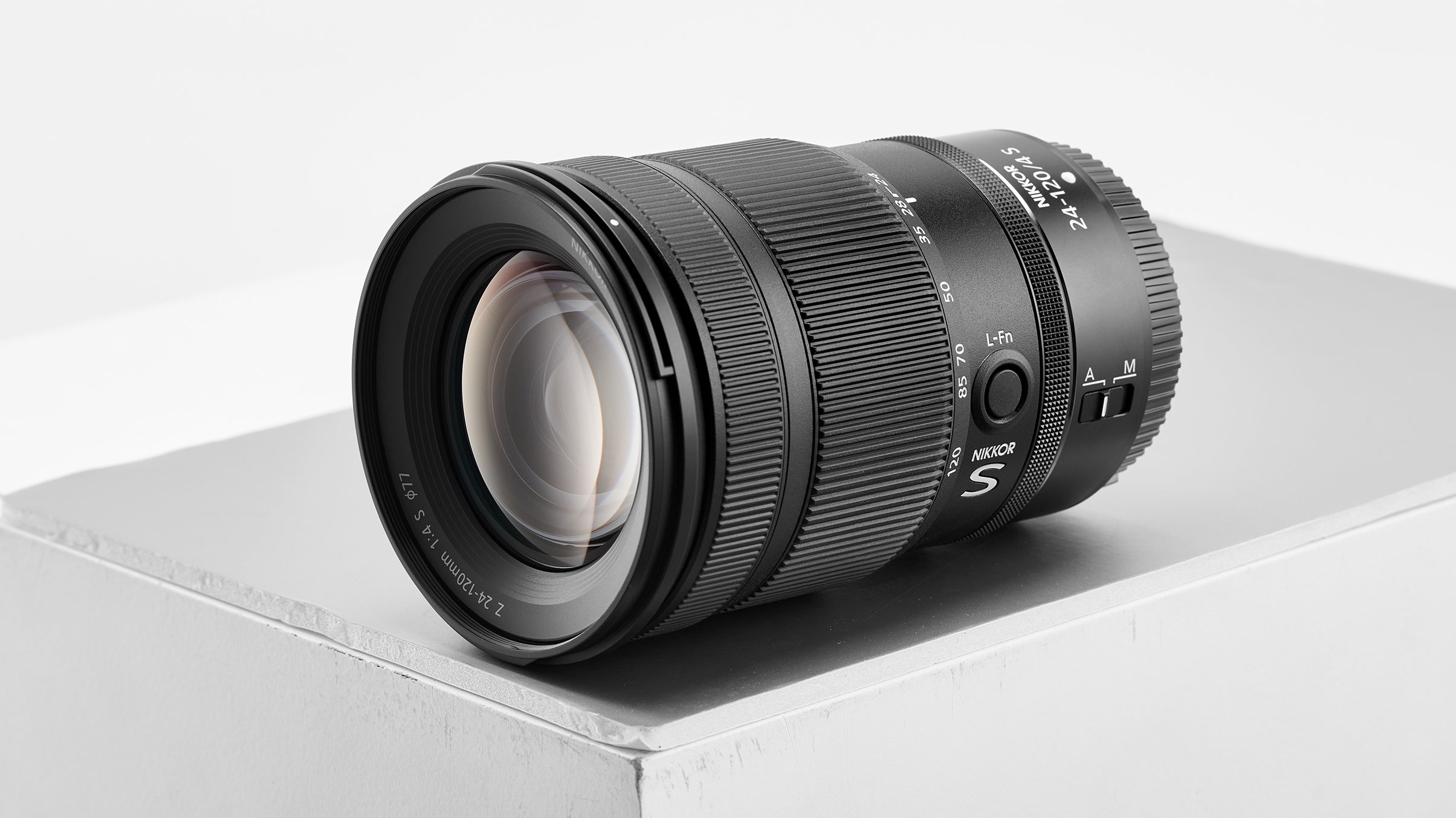 A Nikon Z 24-120mm lens resting on a minimalist gray pedestal, showcasing its sleek design and intricate details
