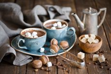 Hot chocolate in mugs with marshmallows, macarons and tea pot